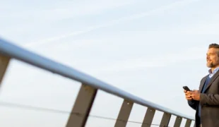 Dirigeant d'entreprise souriant à l'extérieur, consultant son smartphone pour anticiper sa transition et la retraite du dirigeant